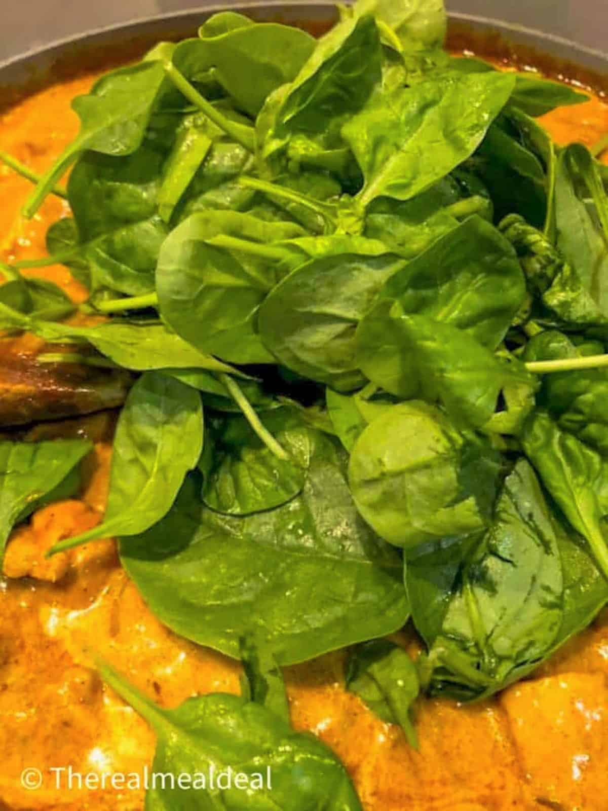 chicken korma in pan with fresh spinach on top