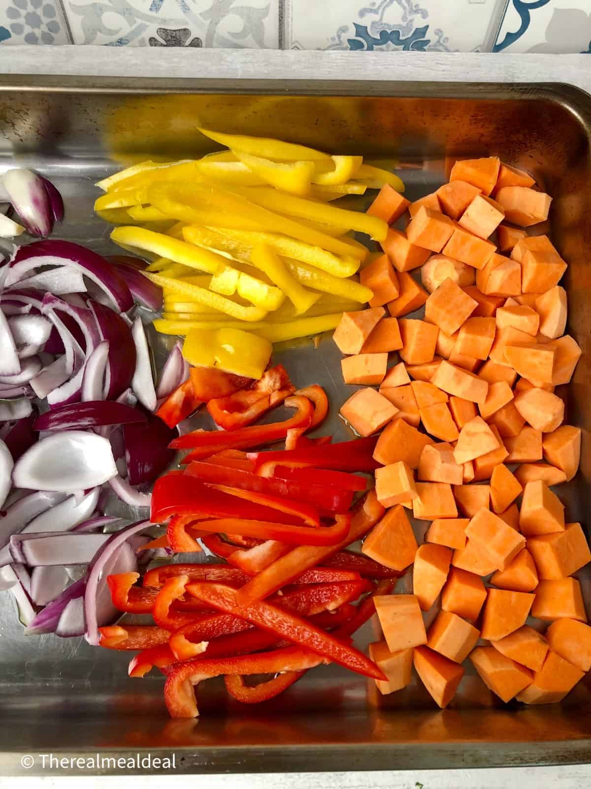sliced peppers red onion and diced sweet potatoes in roasting tin