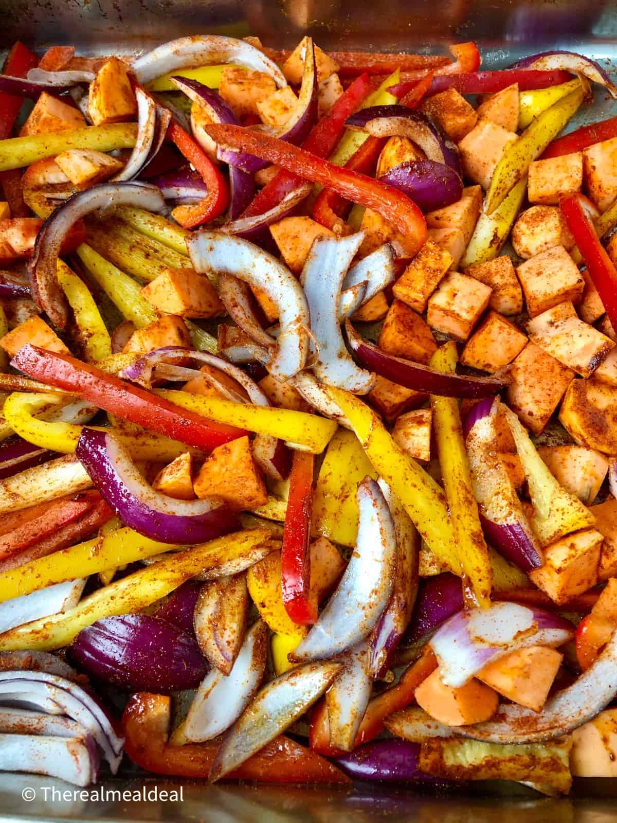 sliced red and yellow peppers red onion diced sweet potato coated in spice mix in roasting tray