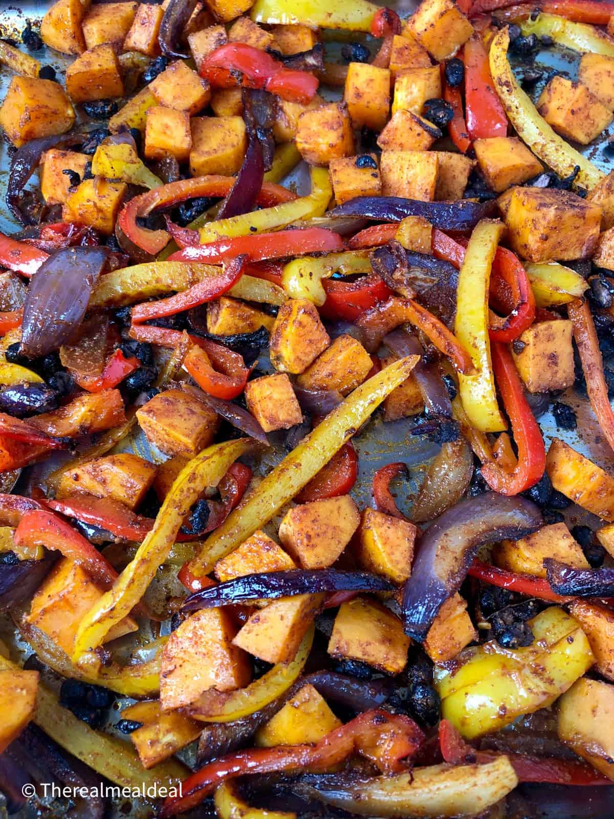 Roasted red and yellow peppers red onions sweet potatoes and black beans in a tray