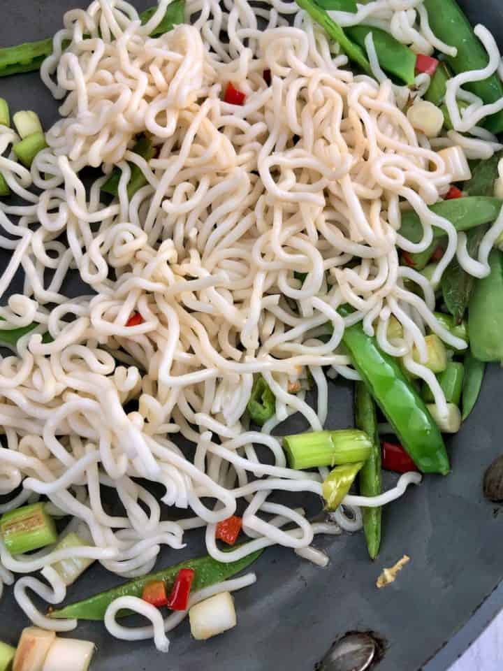 noodles added to spring onions red chilli and mangetout in pan