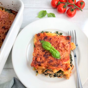 Spinach and Ricotta lasagne portion on plate with fork cherry tomatoes and basil leaves in background