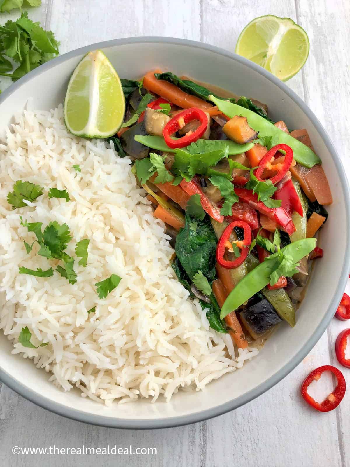 thai vegetable curry in bowl with white rice topped fresh coriander leaves and red chilli slice lime