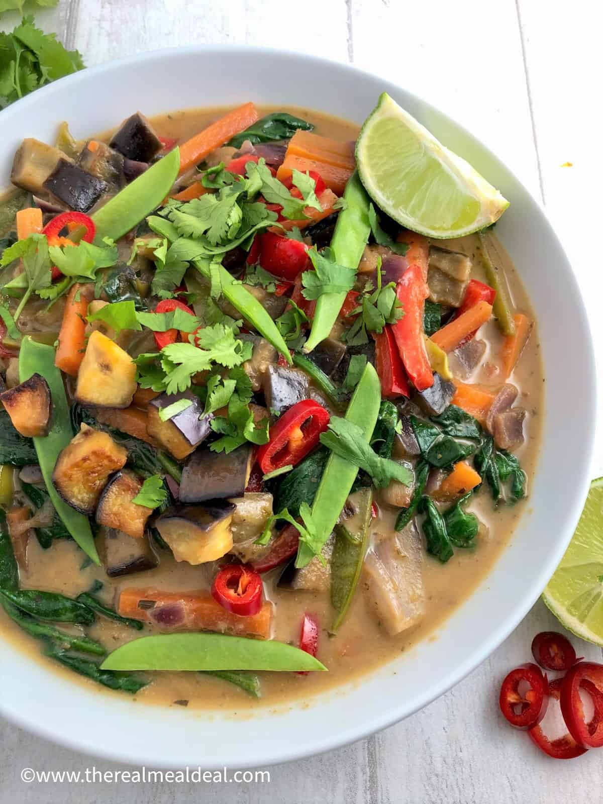 Thai vegetable green curry in bowl topped with fresh coriander red chilli and slice lime