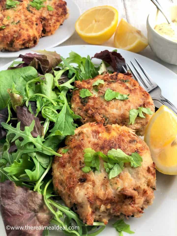tuna fishcakes on plate with green salad and lemon half plate fishcakes lemon halves tartare sauce in background
