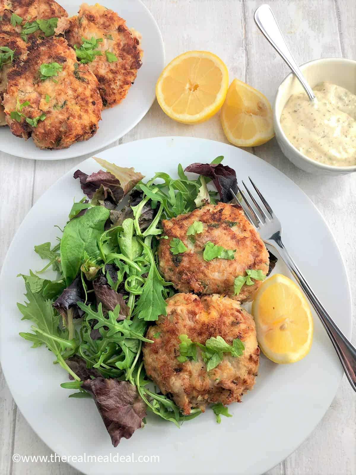 tuna fishcakes on plate with green salad and lemon half plate fishcakes lemon halves tartare sauce in background