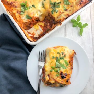vegetable lasagne in tray with portion plated to side topped with fresh basil leaves
