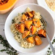 butternut squash risotto in bowl with fresh thyme parmesan half butternut squash and parmesan cheese to side