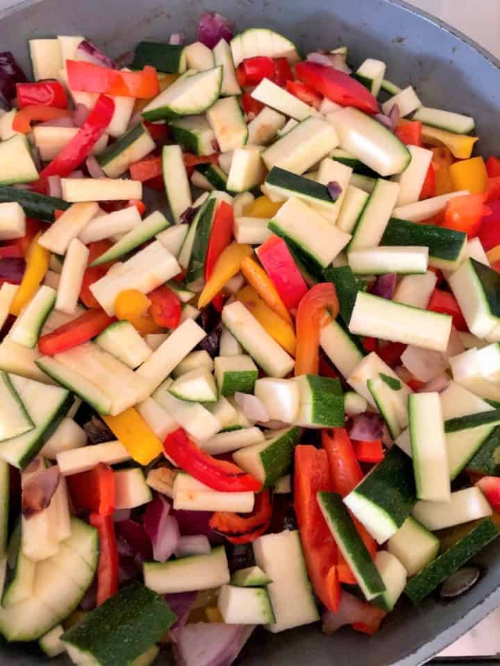 red onion red and yellow peppers and courgette frying in pan
