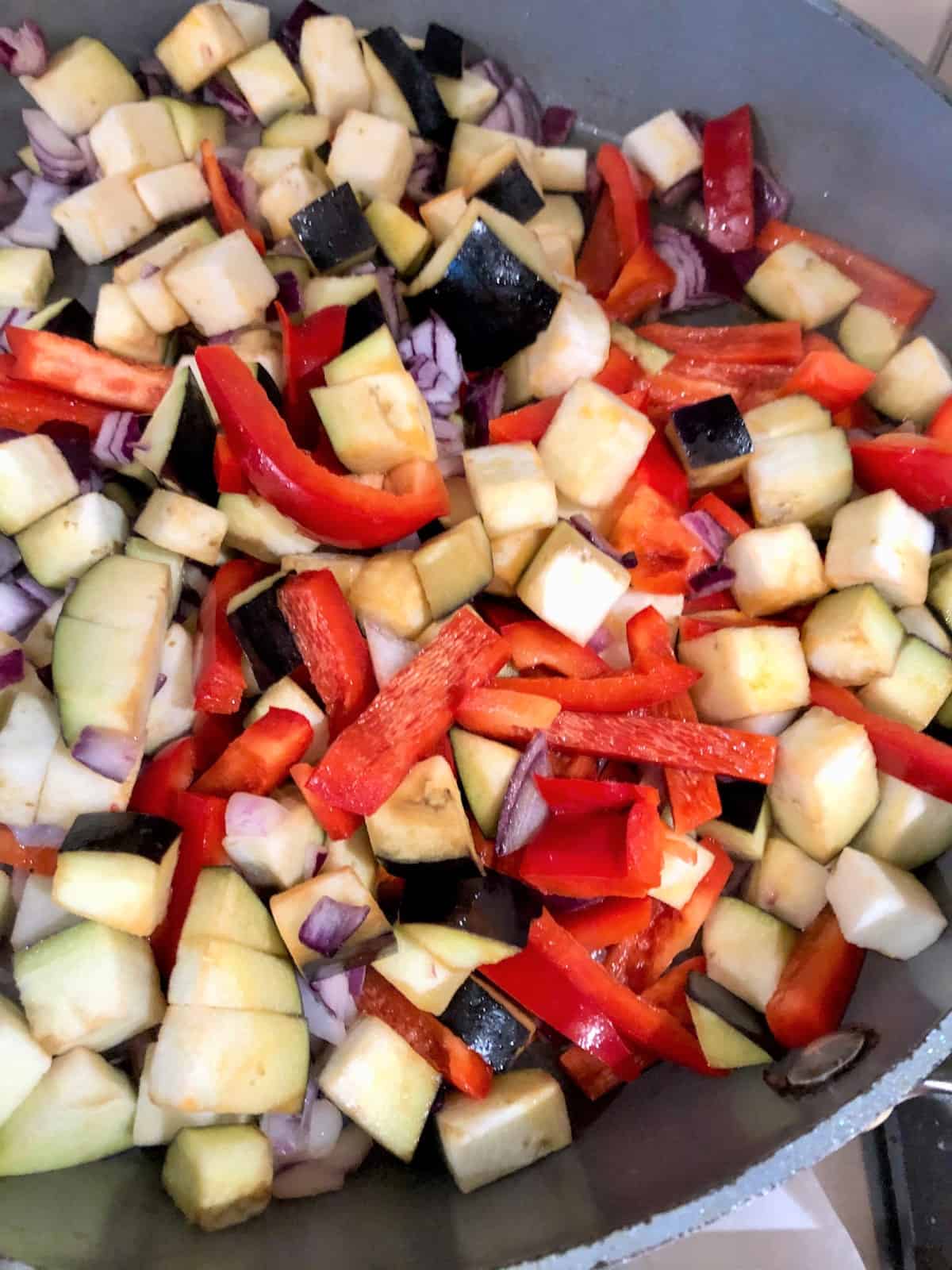 diced red onions red peppers aubergine in frying pan