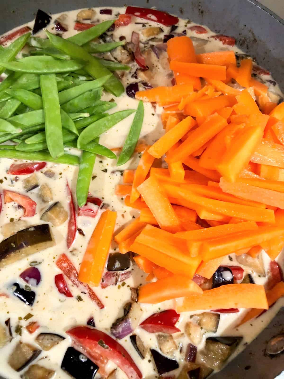 sliced carrots mangetout coconut milk added to pan with red onion red pepper and aubergine