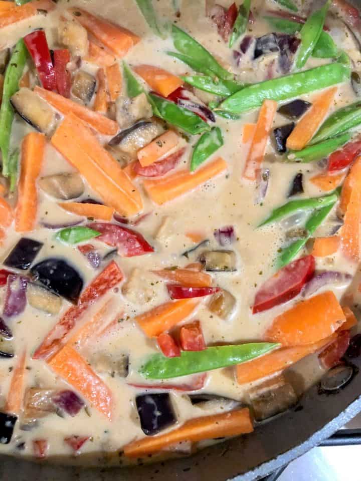 red onion red pepper aubergine carrots mangetout simmering in coconut milk in pan