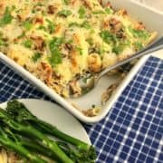 smoked mackerel pasta bake in dish topped with fresh parsley leaves with portion removed and on plate to side with broccoli
