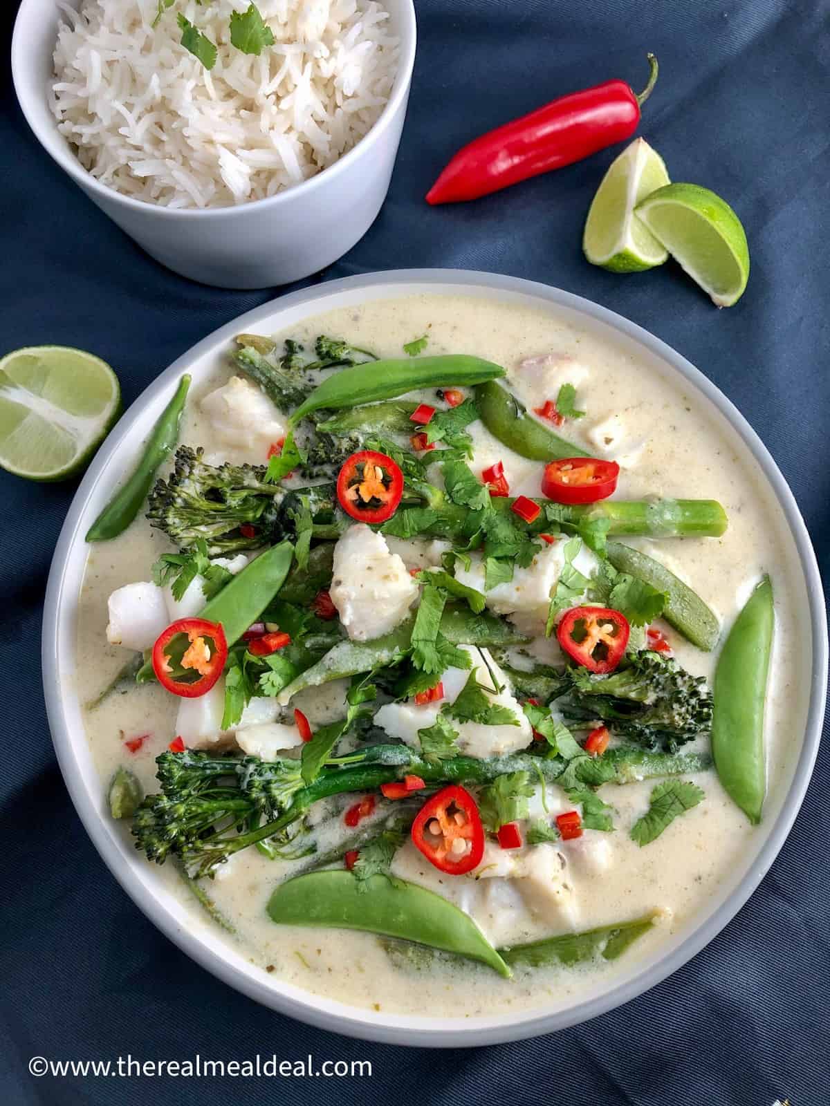thai green fish curry in bowl topped with coriander leaves and red chilli bowl of rice and lime wedge and whole red chilli to side