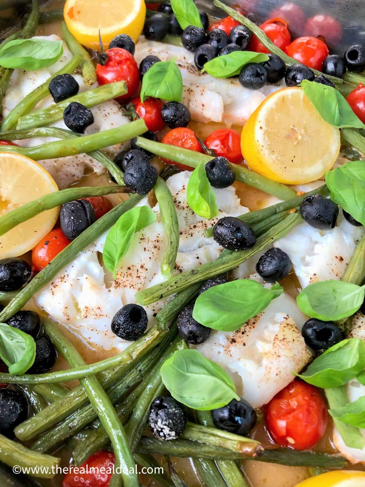 baked cod black olives green beans cherry tomatoes lemon halves and basil leaves in tray