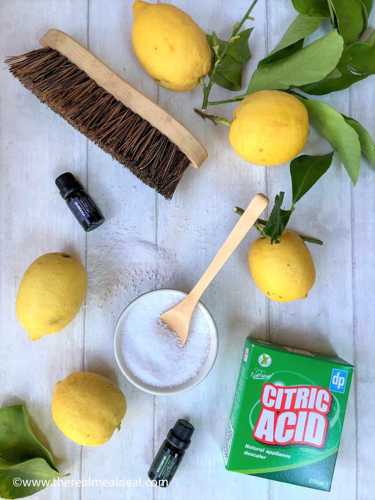 eco cleaning ingredients fresh lemons citric acid lavender oil tea tree oil dishwasher salt in bowl in centre and hard bristle wooden brush