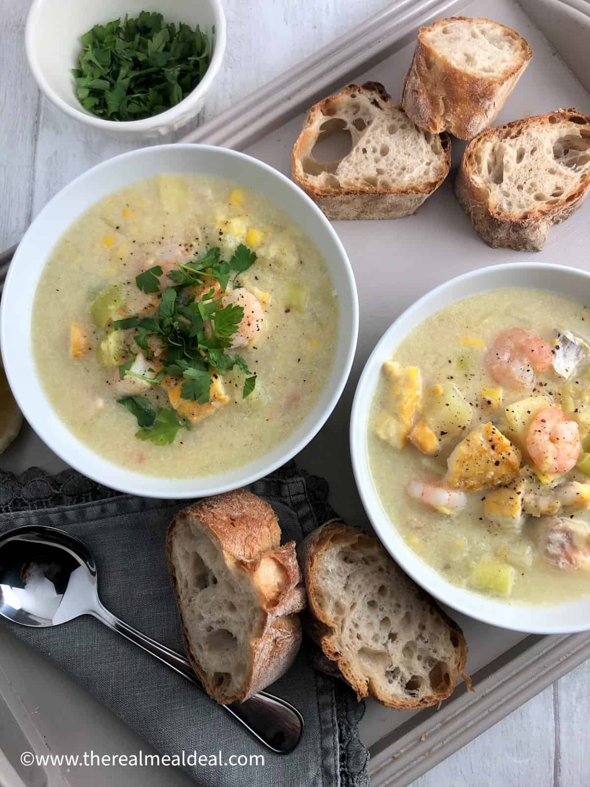 two bowls of smoked haddock and prawn chowder on a tray with sliced baguette