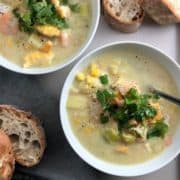 two bowls of smoked haddock and prawn chowder on a tray with sliced baguette