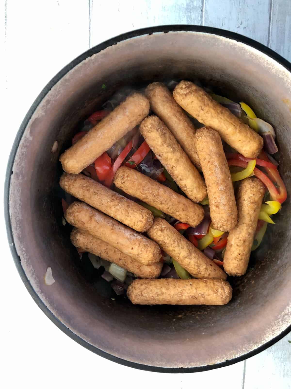 vegan sausages added to red onion peppers and thyme in casserole dish
