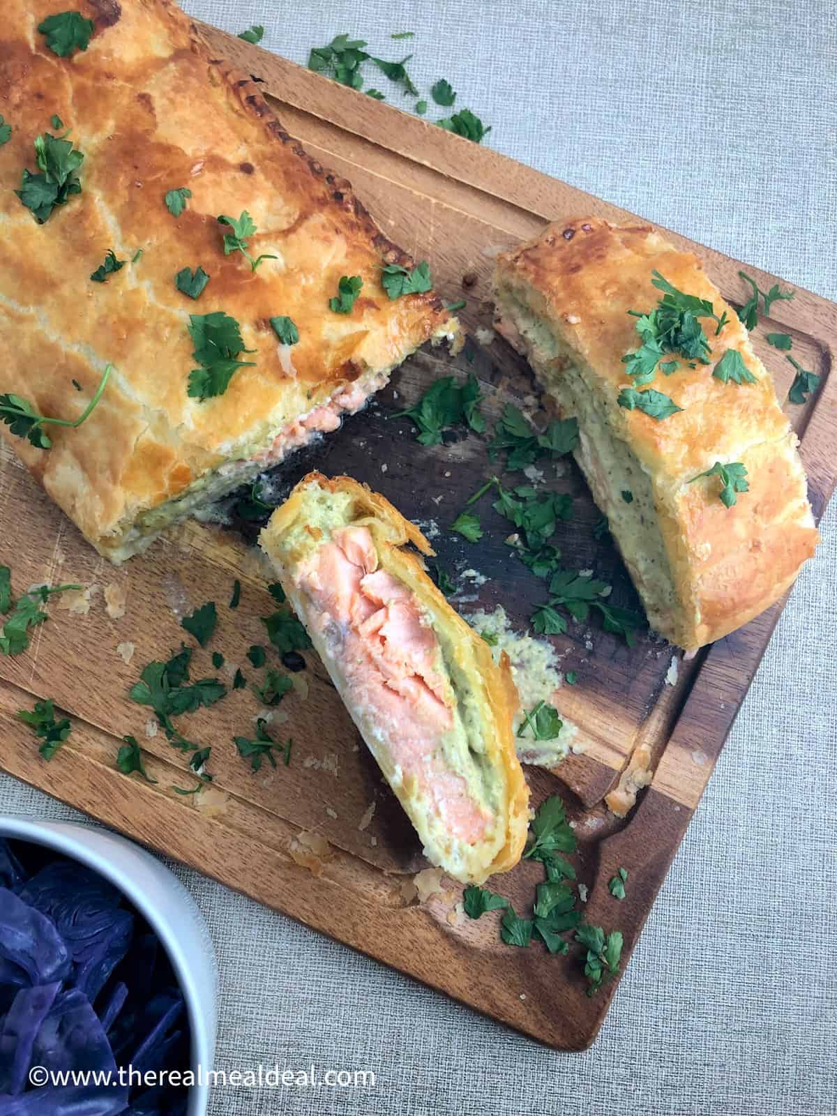 sliced salmon en croute on wooden board showing inside with cooked salmon and cream cheese and spinach