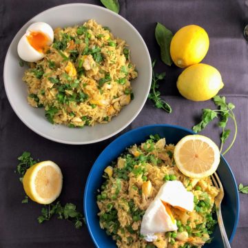 two bowls of kedgeree with smoked haddock topped with poached and boiled egg and served with chopped parsley and lemon halves