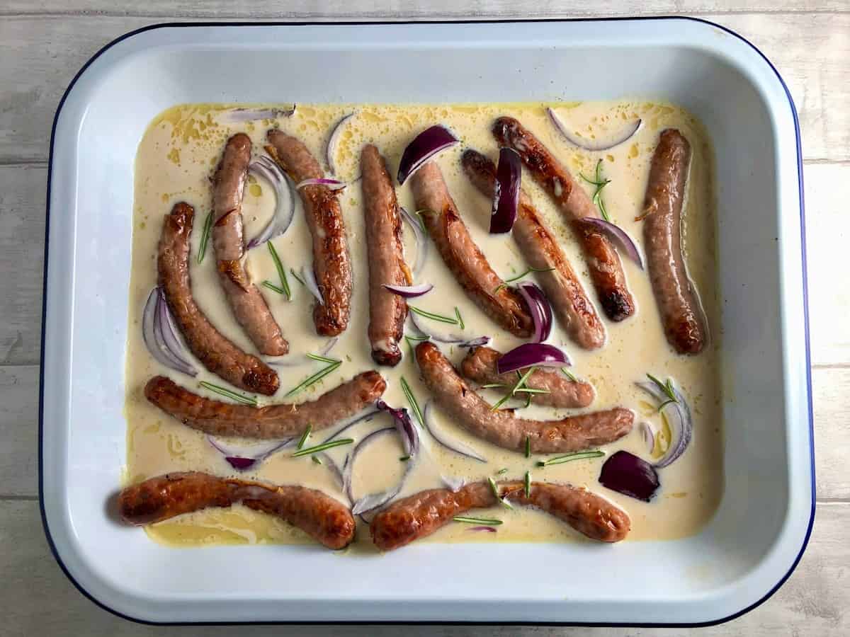 sausages in metal tray with batter mix red onion and rosemary