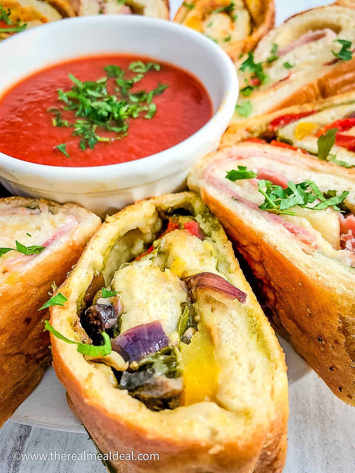 close up of stromboli pizza slices with various fillings on plate with dipping sauce