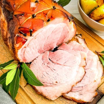 honey roast gammon joint on board, showing slices with bowl of roast potatoes to side