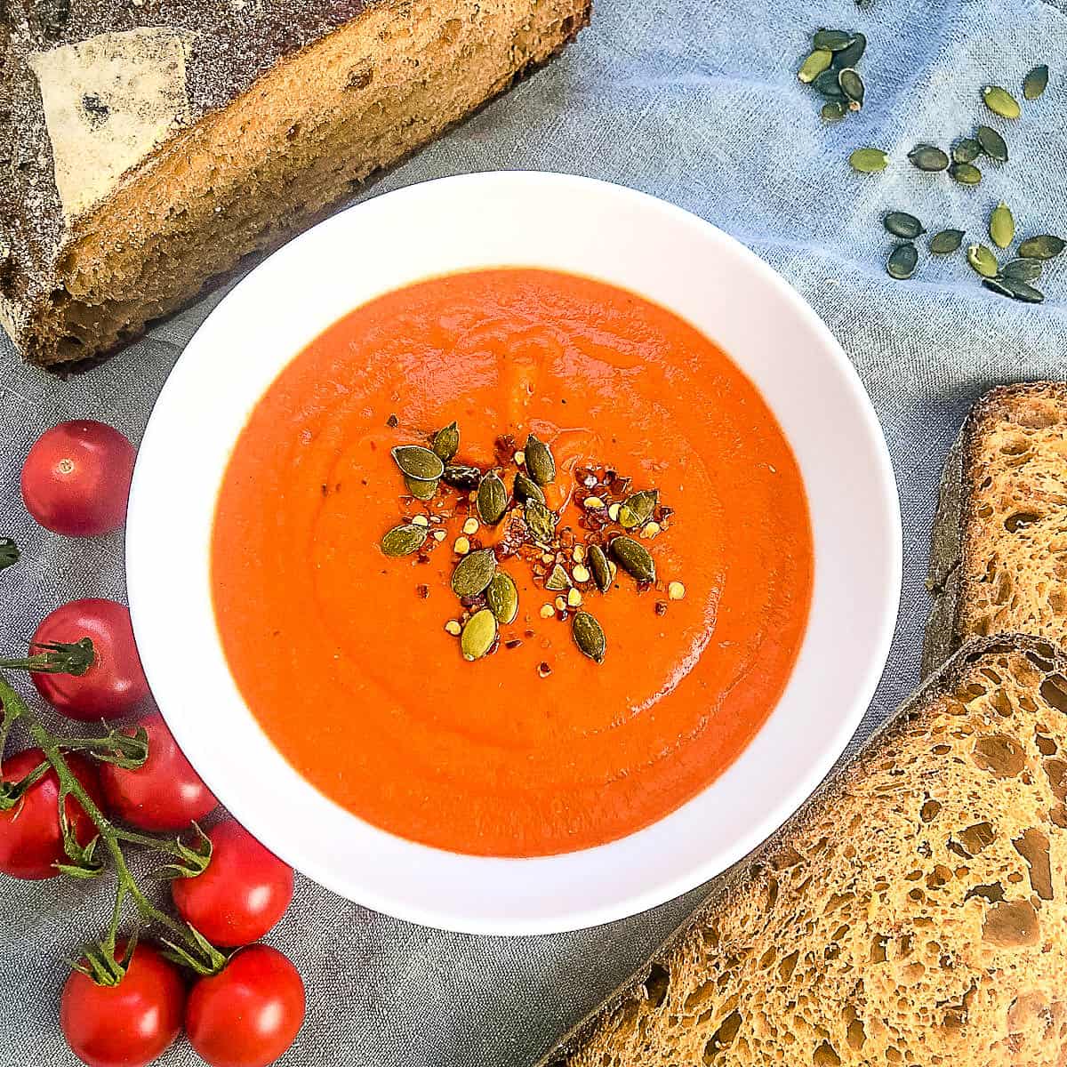 bowl of roasted red pepper and lentil soup garnished with pumpkin seeds and chilli flakes.