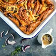 vegan toad in the hole in metal tray with onion gravy to side