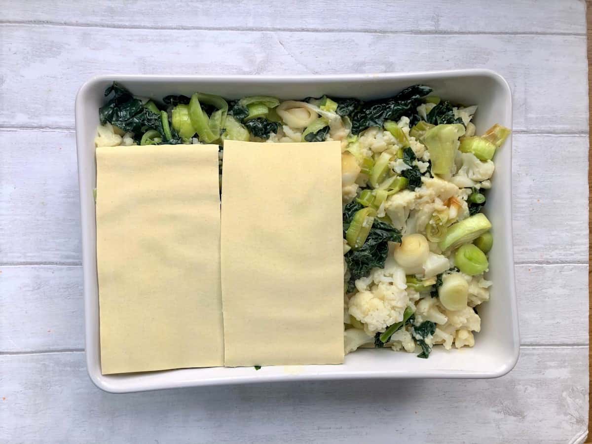 cauliflower leek and kale lasagne being assembled in dish showing vegetables and lasagne sheets on top