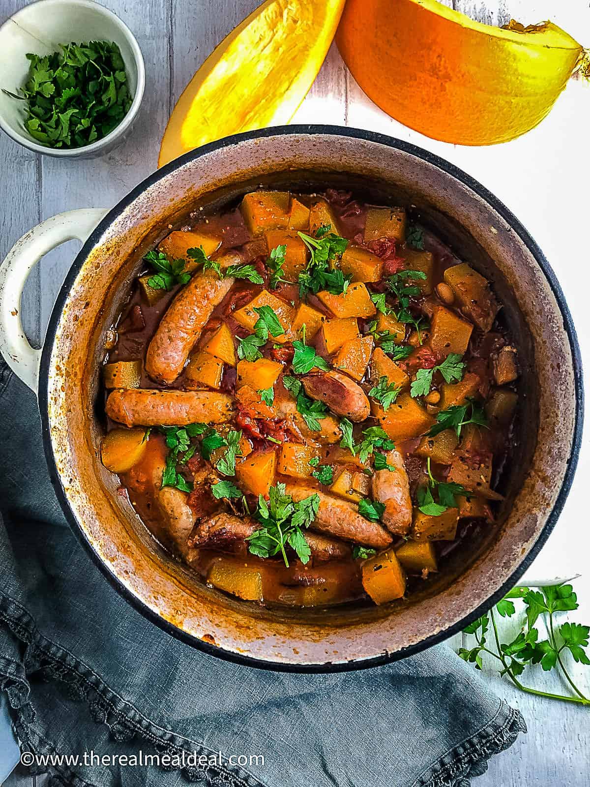 sausage and baked bean casserole with pumpkin in dish topped with fresh parsley