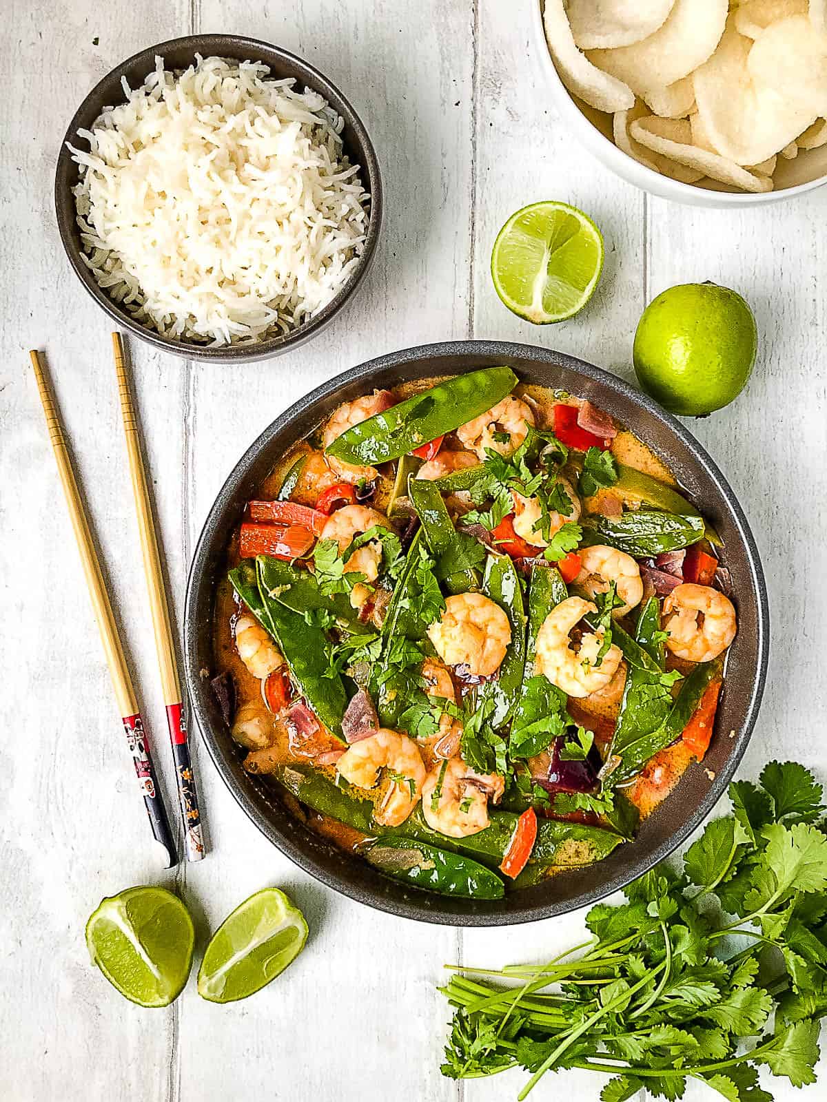 thai prawn red curry in bowl with chopsticks and bowl of rice to side with lime quarters.