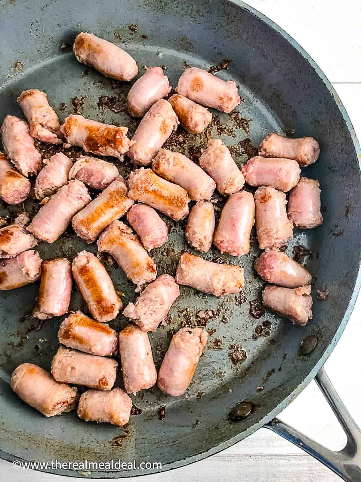 sausages cut into bite sized pieces frying in pan.