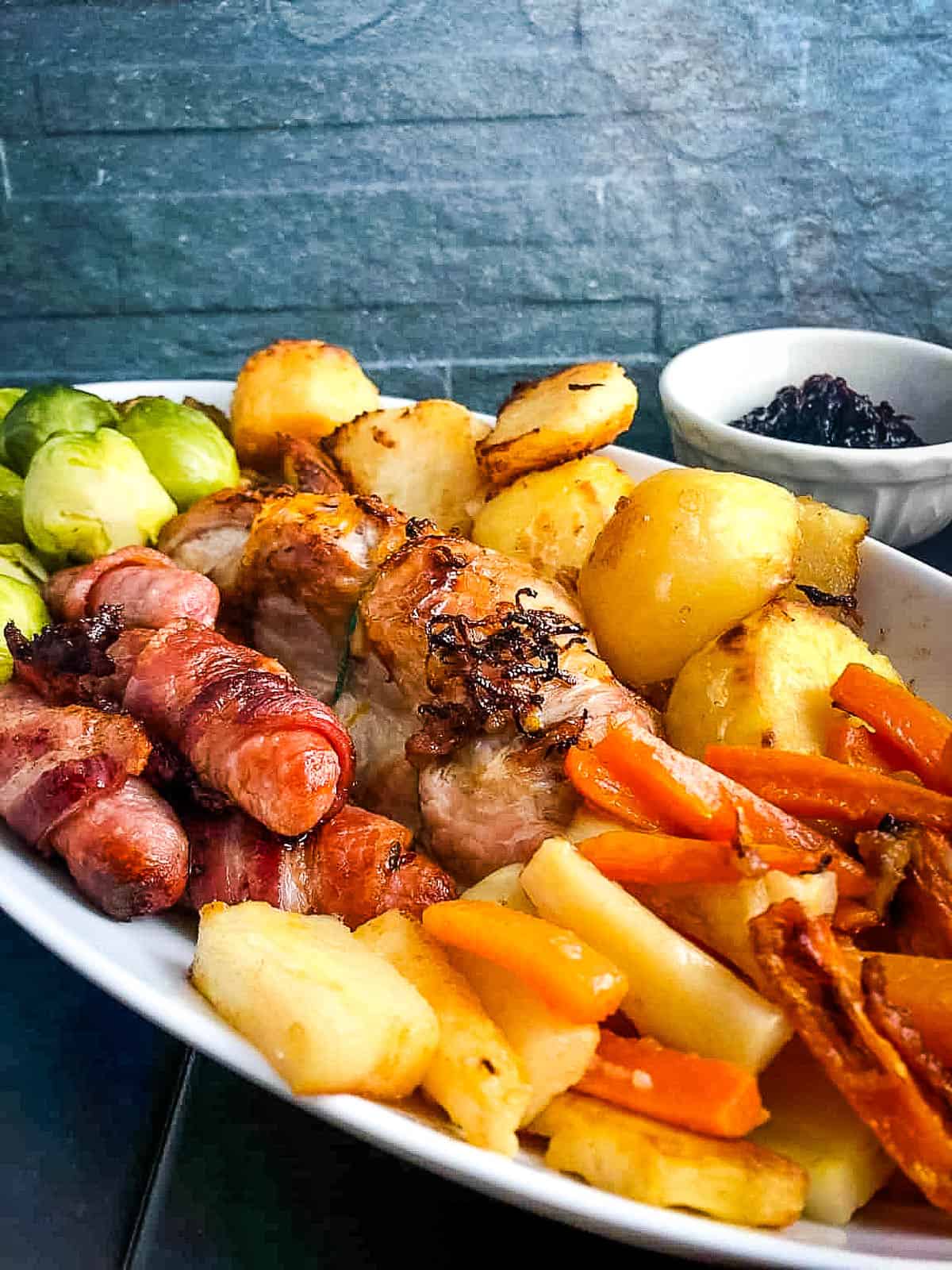 turkey breast pigs in blankets roast potatoes carrots parsnips sprouts on plate with side of cranberry sauce