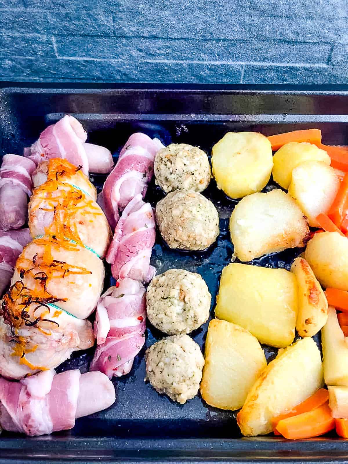 turkey breast pigs in blankets stuffing balls roast potatoes carrots and parsnips in tray.