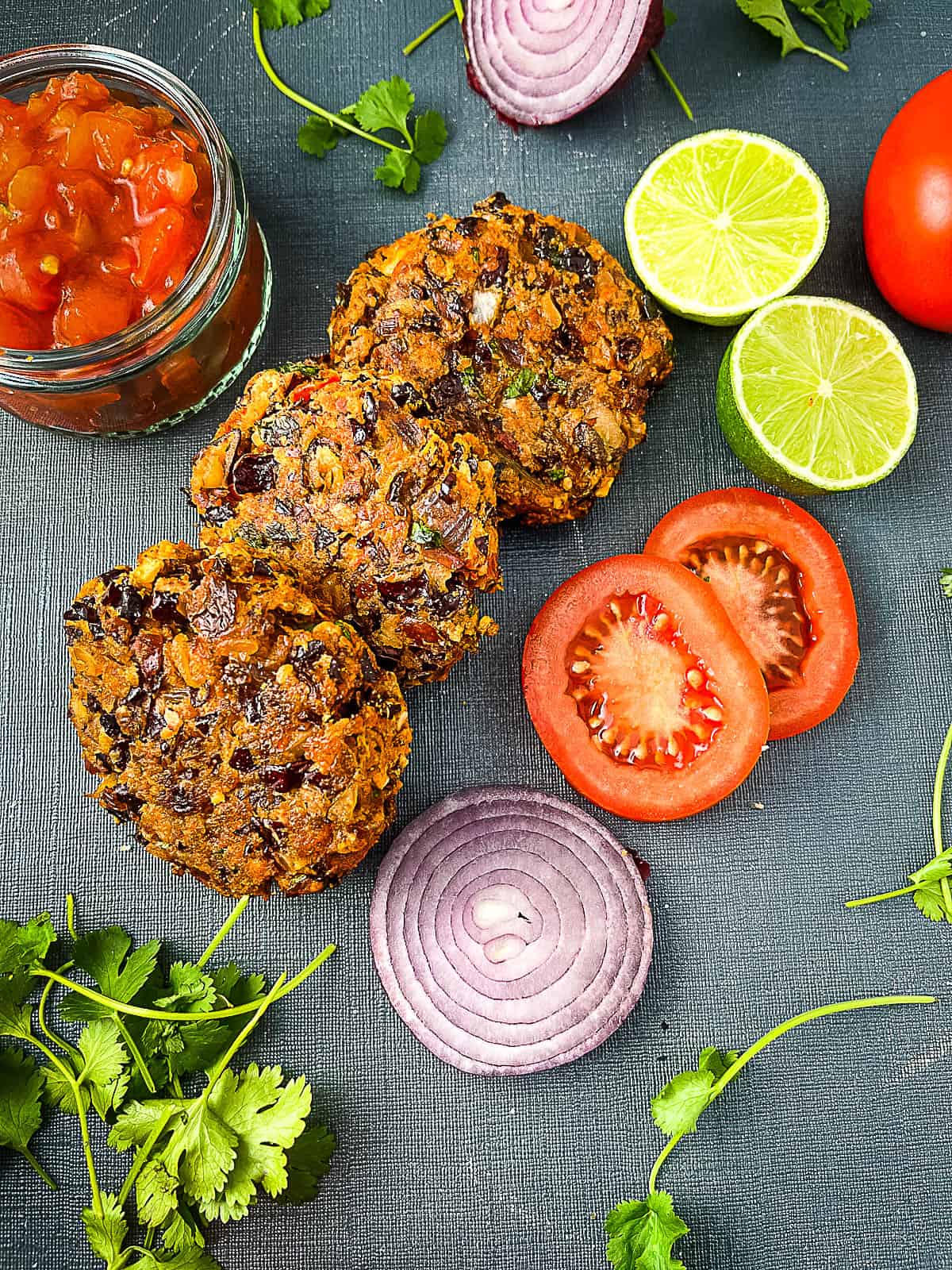 red kidney bean burger with sides of salsa, limes tomato and red onion