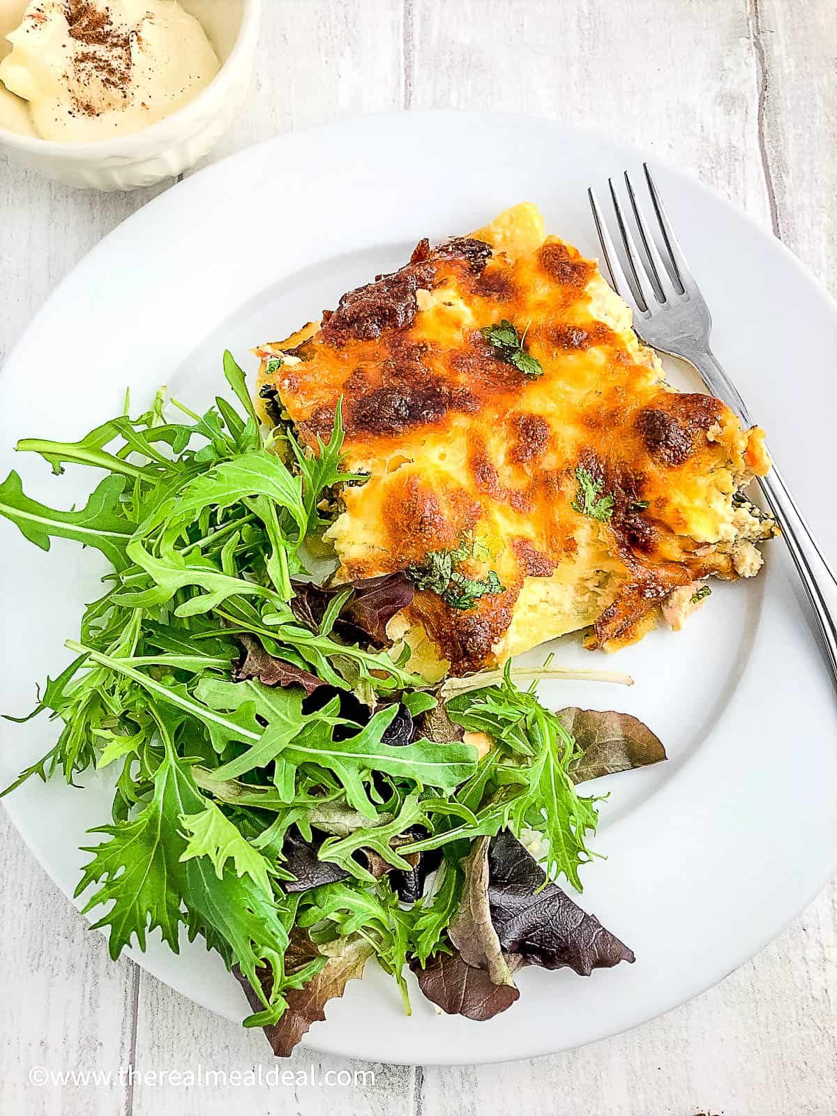 portion of salmon lasagne with spinach on plate with green salad