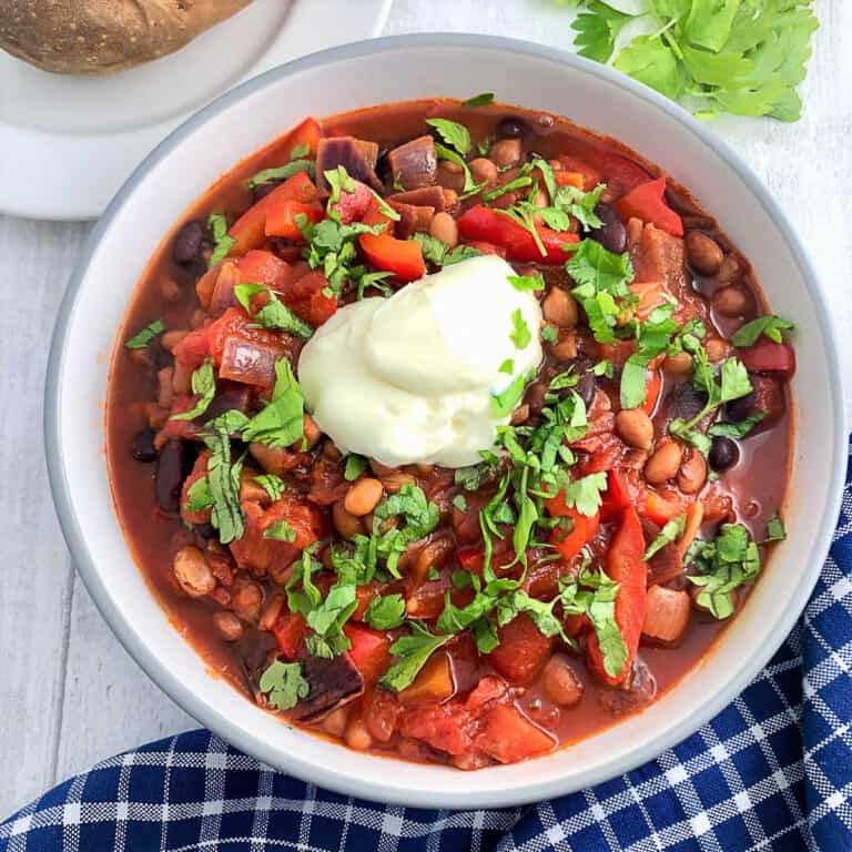 bowl of bean goulash topped with soured cream and fresh parsley