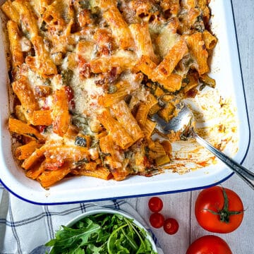 vegetable and pesto pasta bake finished dish with portion removed and side of green salad and tomatoes
