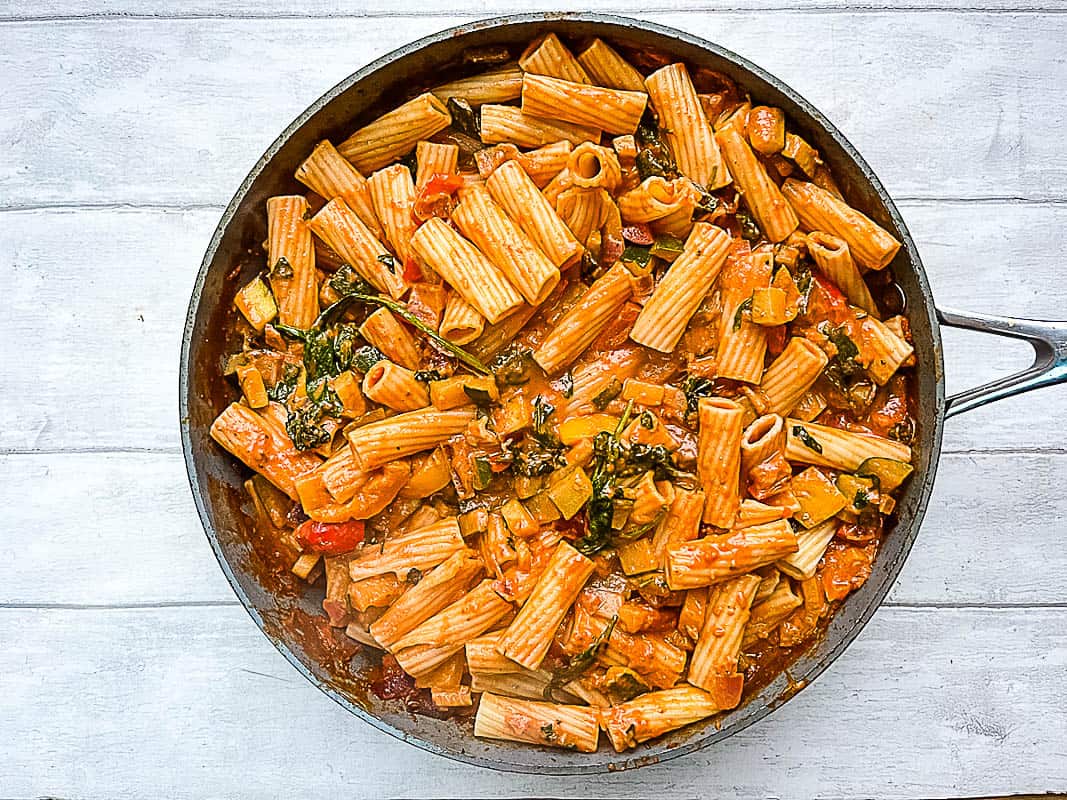 pasta noodles added to vegetables, passata and red pesto in pan