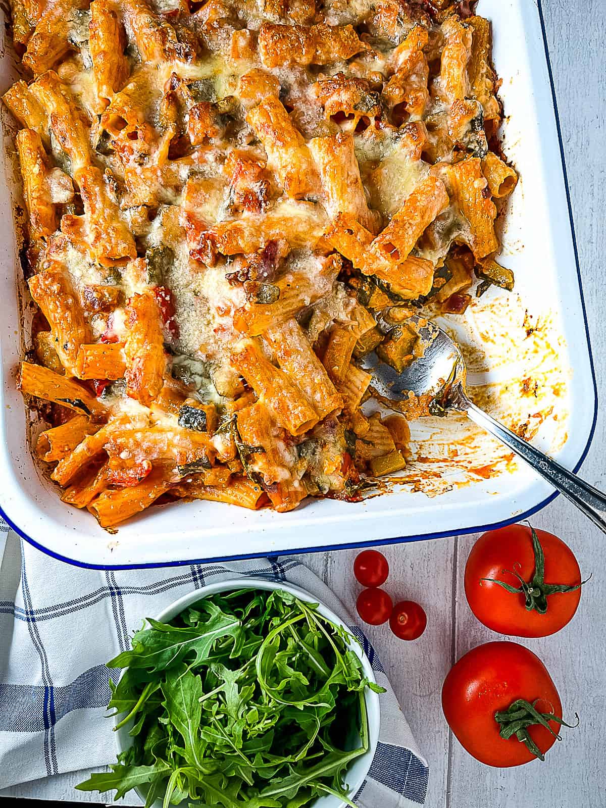 vegetable and pesto pasta bake in dish with portion removed and side green salad and fresh tomatoes