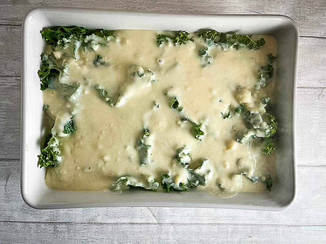 cheesy bechamel sauce poured over kale and fish in dish