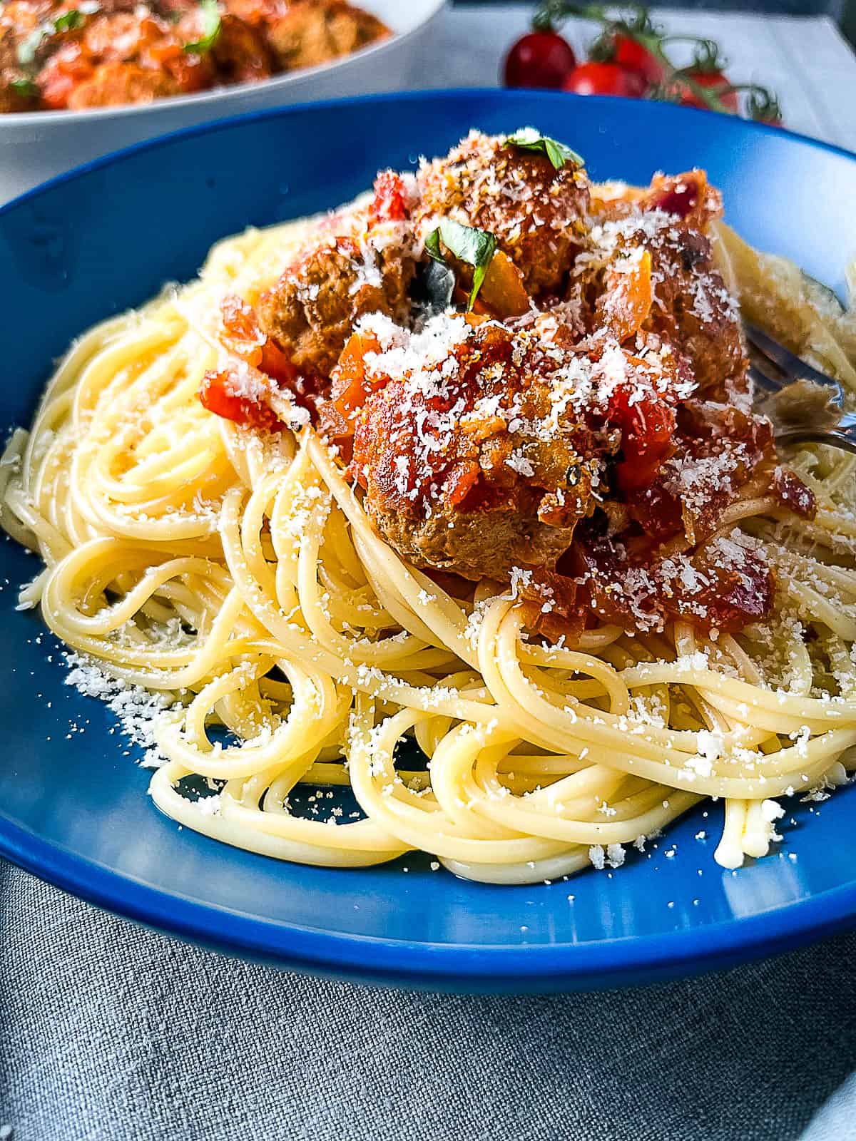 close up of pork meatballs over spaghetti topped ith parmesan cheese