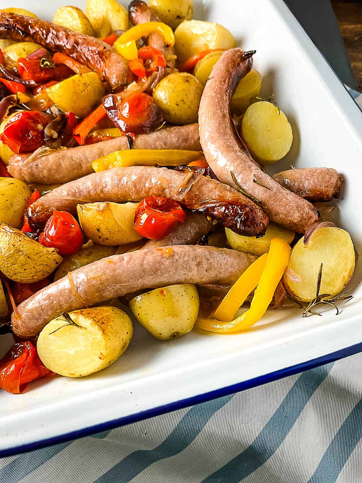 sticky sausage tray bake in tray topped with fresh rosemary