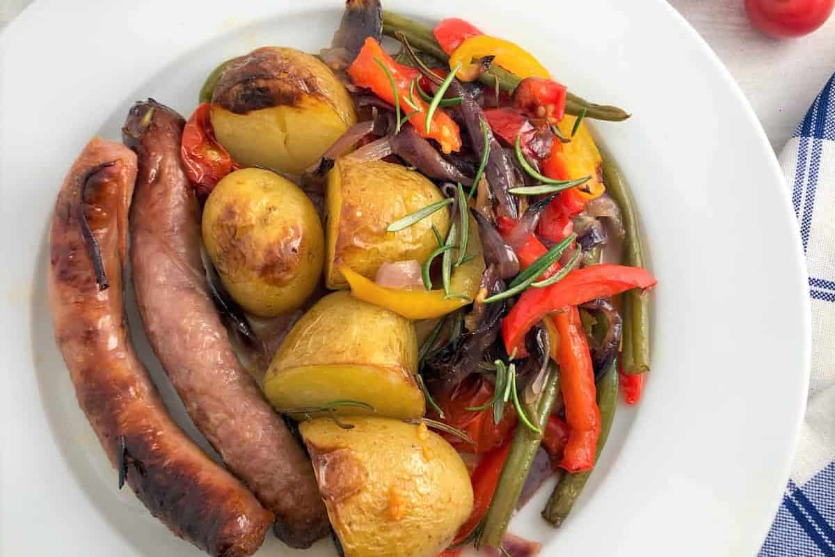 sausage tray bake with red onions peppers and potatoes served on a plate