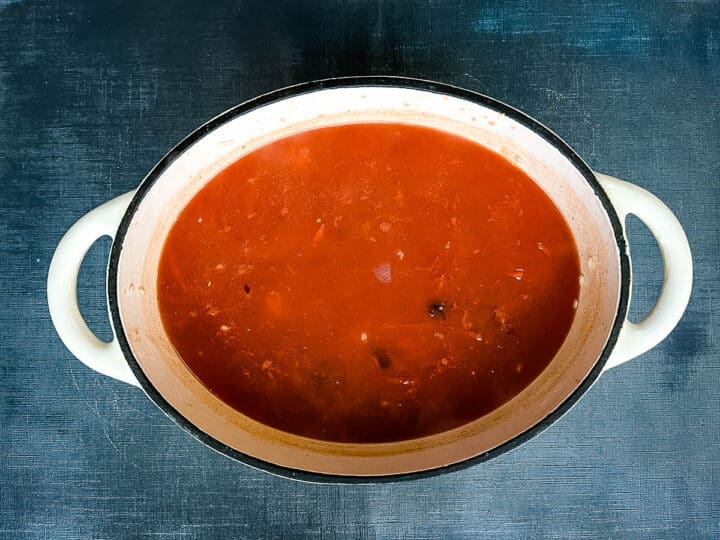 stock and tinned tomatoes added to risotto rice in pan