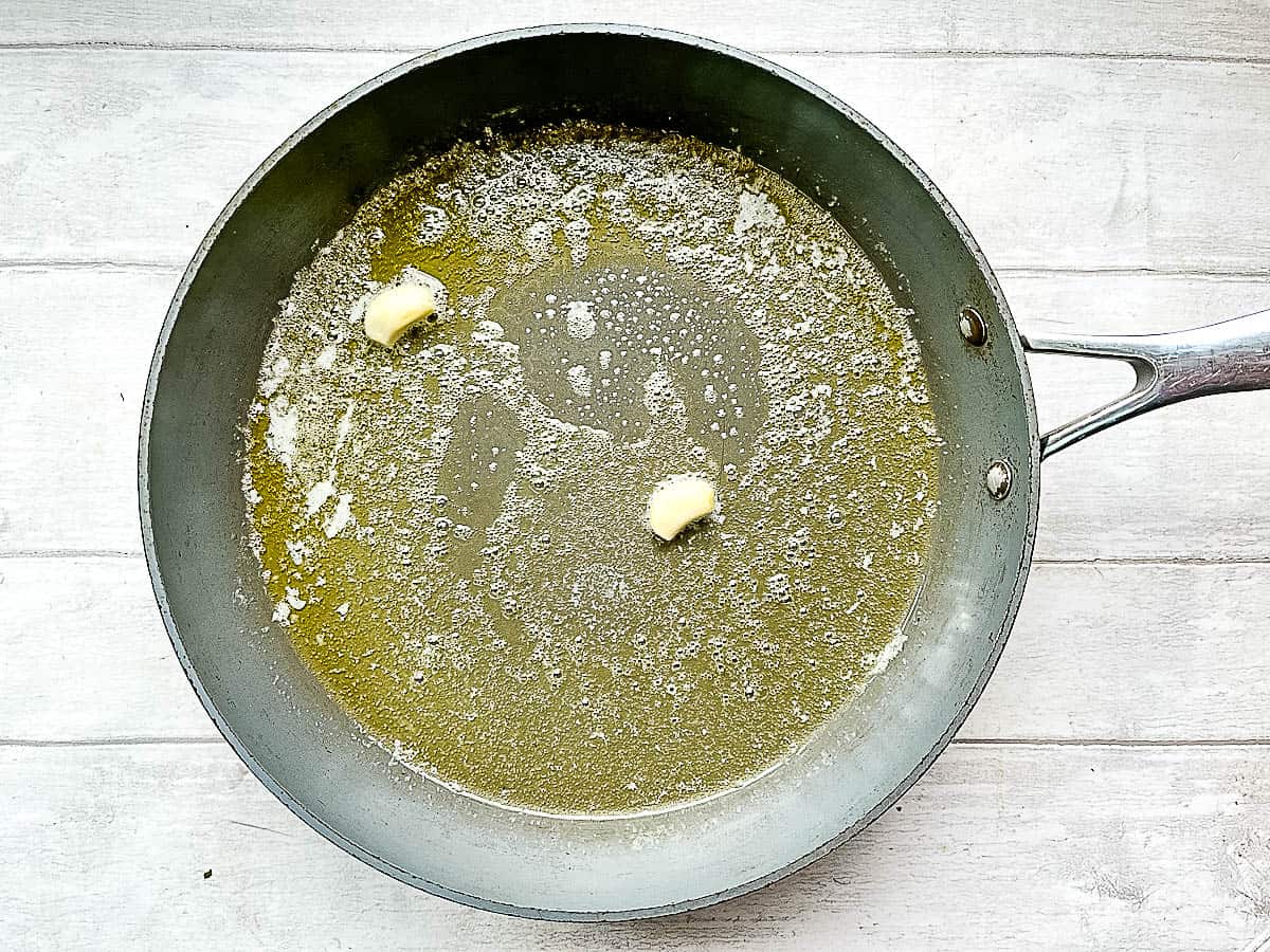 butter melting in pan with two garlic cloves.