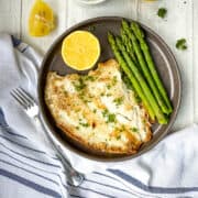 plaice fillet fried in butter on plate with asparagus and lemon.