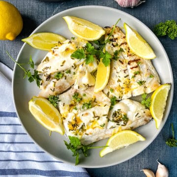 baked haddock fillets on plate with lemon wedges.